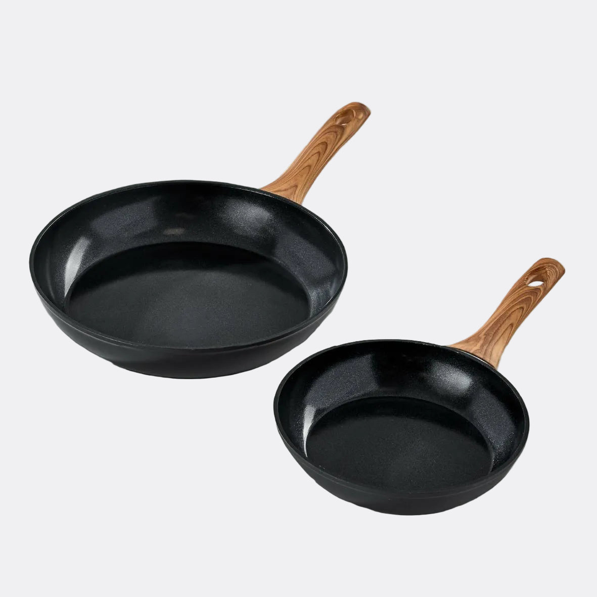 Two black frying pans with wooden handles on a light grey background