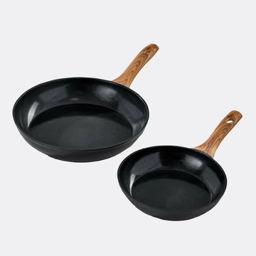 Two black frying pans with wooden handles on a light grey background
